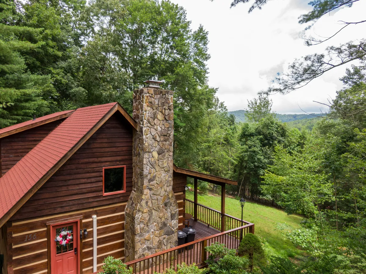 This image features the exterior of Moonlight Lodge, showcasing a charming stone chimney, a red front door, and an inviting wooden deck surrounded by trees. The setting is serene and connected to nature, emphasizing the retreat’s peaceful location close to area attractions.