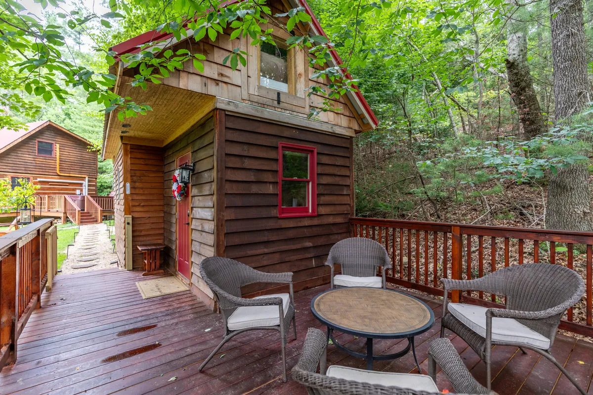 This image shows the rustic exterior of a wooden cabin with a cozy outdoor seating area encircled by trees. The scene conveys relaxation, with guests able to gather and enjoy the natural surroundings, perfect after a day out in town.