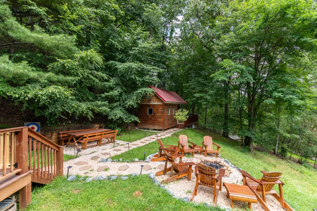 A wooden cabin set amidst the woods, with an inviting fire pit, outdoor seating, and a clear pathway leading into the surrounding forest. The area is ideal for relaxation and for starting a walk through nature.