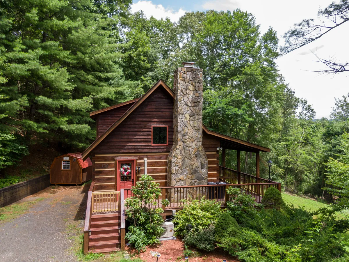 A picturesque log cabin with a stone chimney and deck sits amid lush greenery, complemented by a decorative wreath on the door. The scene suggests a peaceful home base, surrounded by nature and close to hiking trails, ideal for easy outings with kids or pets.