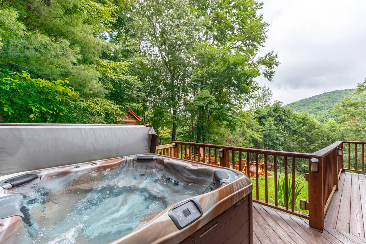 A state-of-the-art hot tub set on a wooden deck, surrounded by lush greenery and offering expansive mountain views. The setting sun casts a gentle glow, creating an inviting space to relax and take in nature.