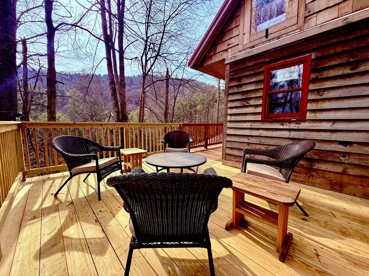 A peaceful private deck with comfortable wicker chairs and a coffee table, looking out onto mountain vistas. The space feels intimate and is ideal for enjoying the outdoors in any season, echoing the guest house deck's role as a quiet retreat.