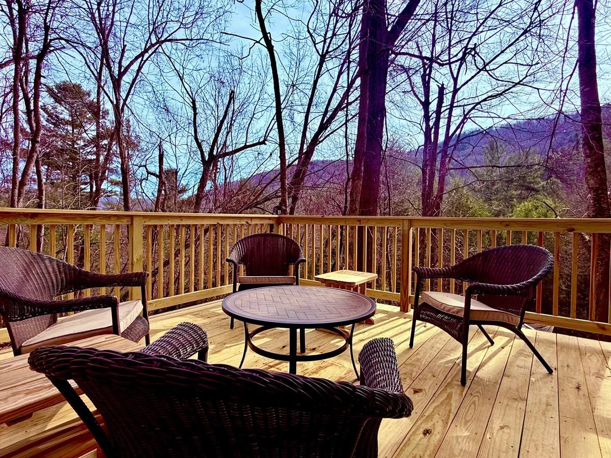 Set on a deck with wicker chairs and a round coffee table, this image offers sweeping views of the surrounding trees and distant mountains. The outdoor space is designed for relaxation, with opportunities for sunset watching or stargazing after a day of town exploration.